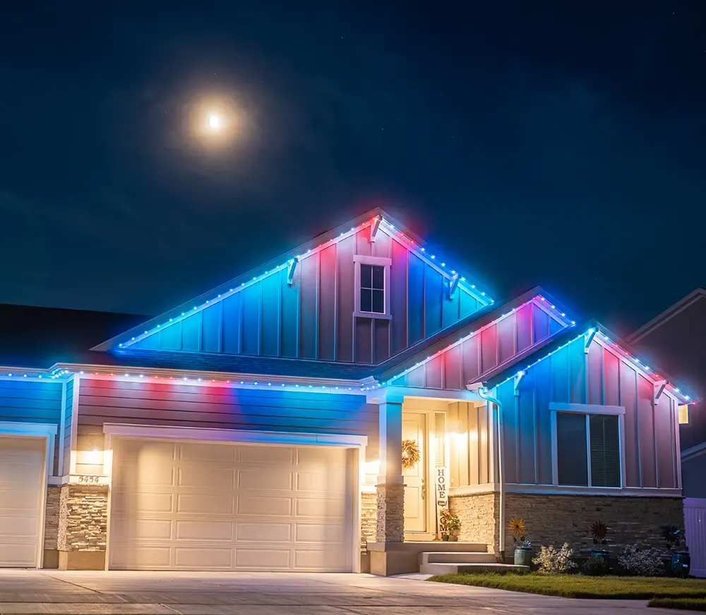Residential home with red, white and blue permanent lights under a full moon